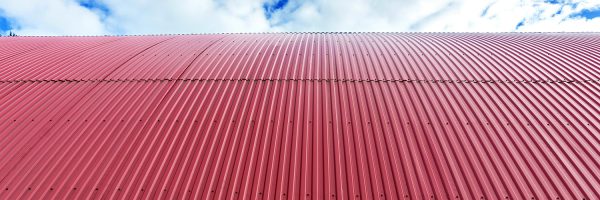 Rooftop of curved red corrugated iron on blue sky with fluffy clouds